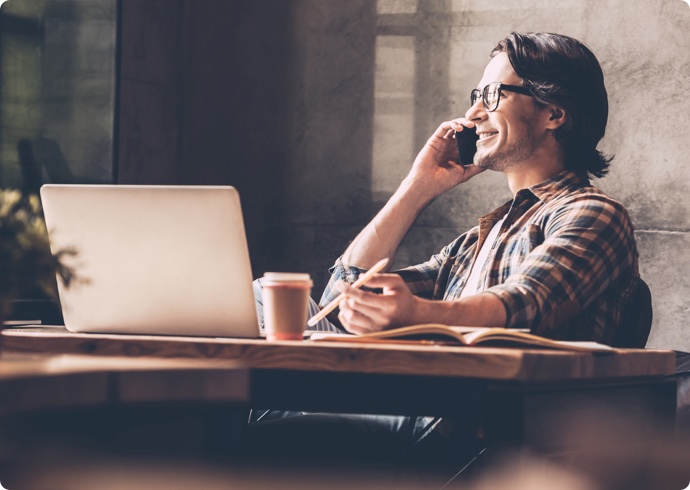 Smiling man talking on cellphone laptop on table
